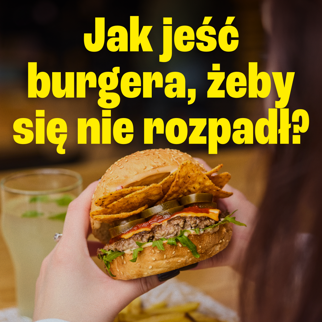 Burger trzymany oburącz z napisem Jak jeść burgera, żeby się nie rozpadł?